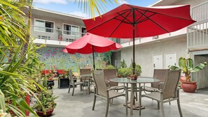 An outdoor patio with a round table and chairs, surrounded by potted plants and a red umbrella. - Ramada Limited Redondo Beach (Redondo Beach)