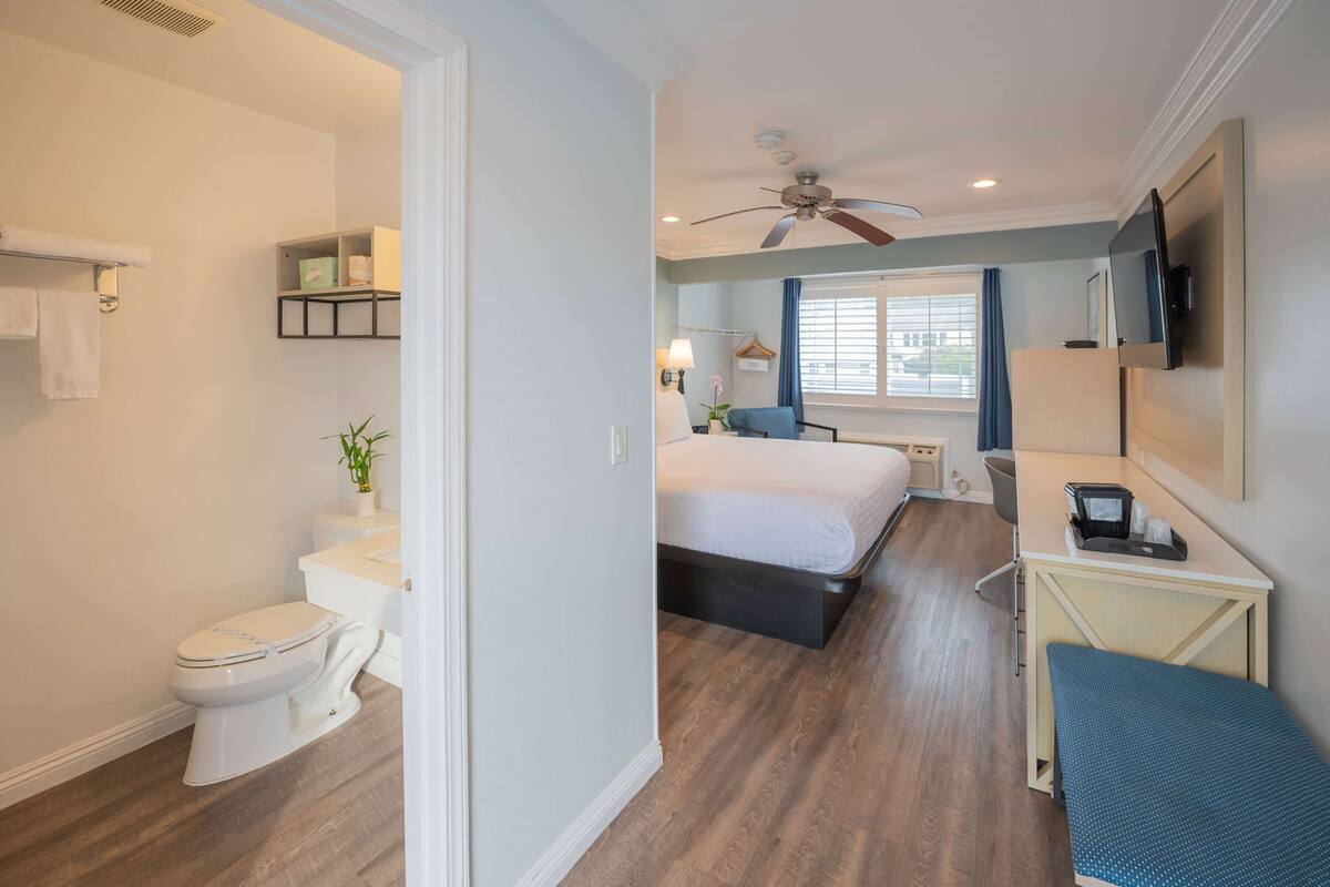 Habitación de hotel con inodoro, lavabo, cama, mesita de noche y televisión.
