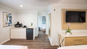 A hotel room with a kitchenette, a TV mounted on the wall, and a bed with a white comforter. - Ramada Limited Redondo Beach (Redondo Beach)