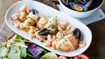 A seafood dish with mussels, shrimp, and salmon, accompanied by a salad and bread.