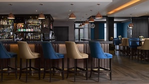 A bar area with multiple stools, a bar counter stocked with bottles, and pendant lighting. - The Galmont (Galway)