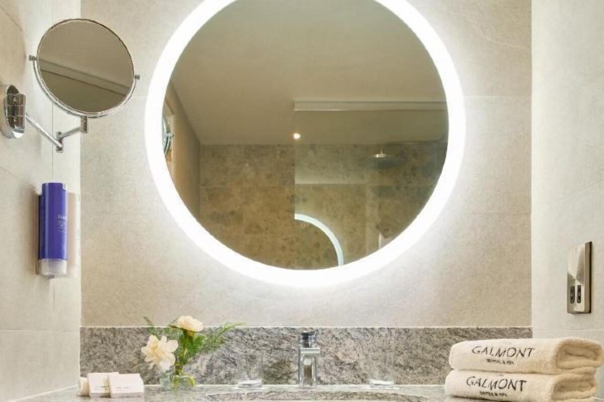 A modern bathroom with a round mirror, a marble sink, and a towel rack with towels.