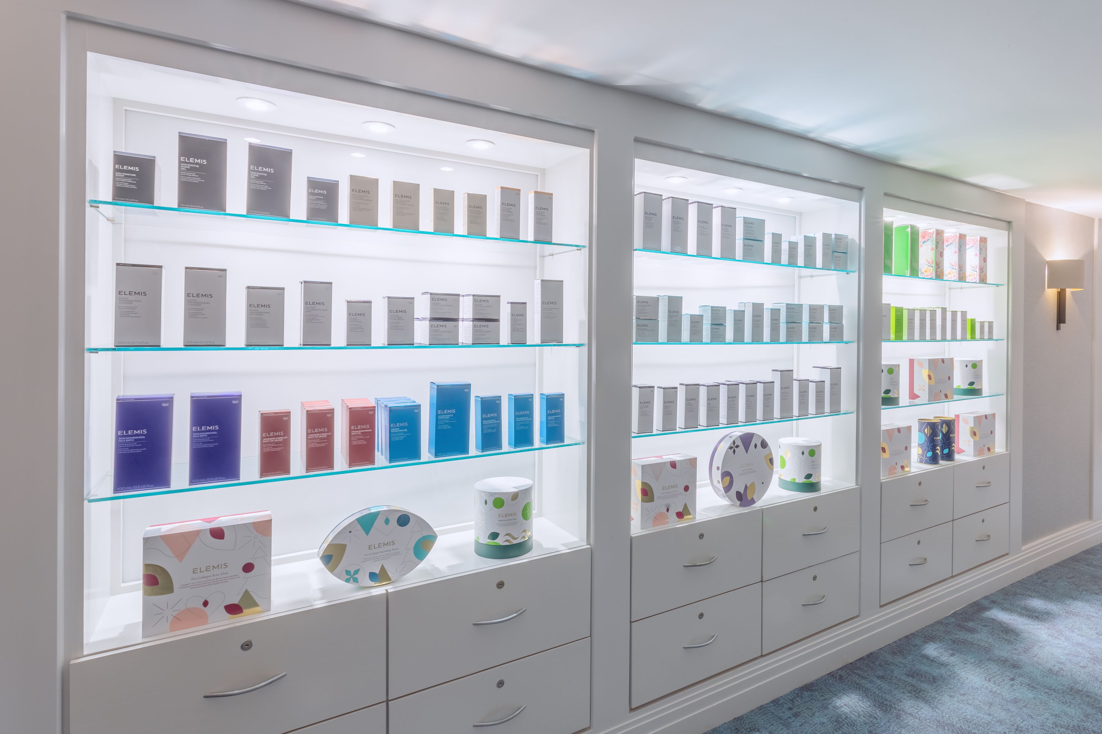 Una presentación de productos de cuidado de la piel Elemis en un gabinete de vidrio bien iluminado, con varios estantes y cajones.