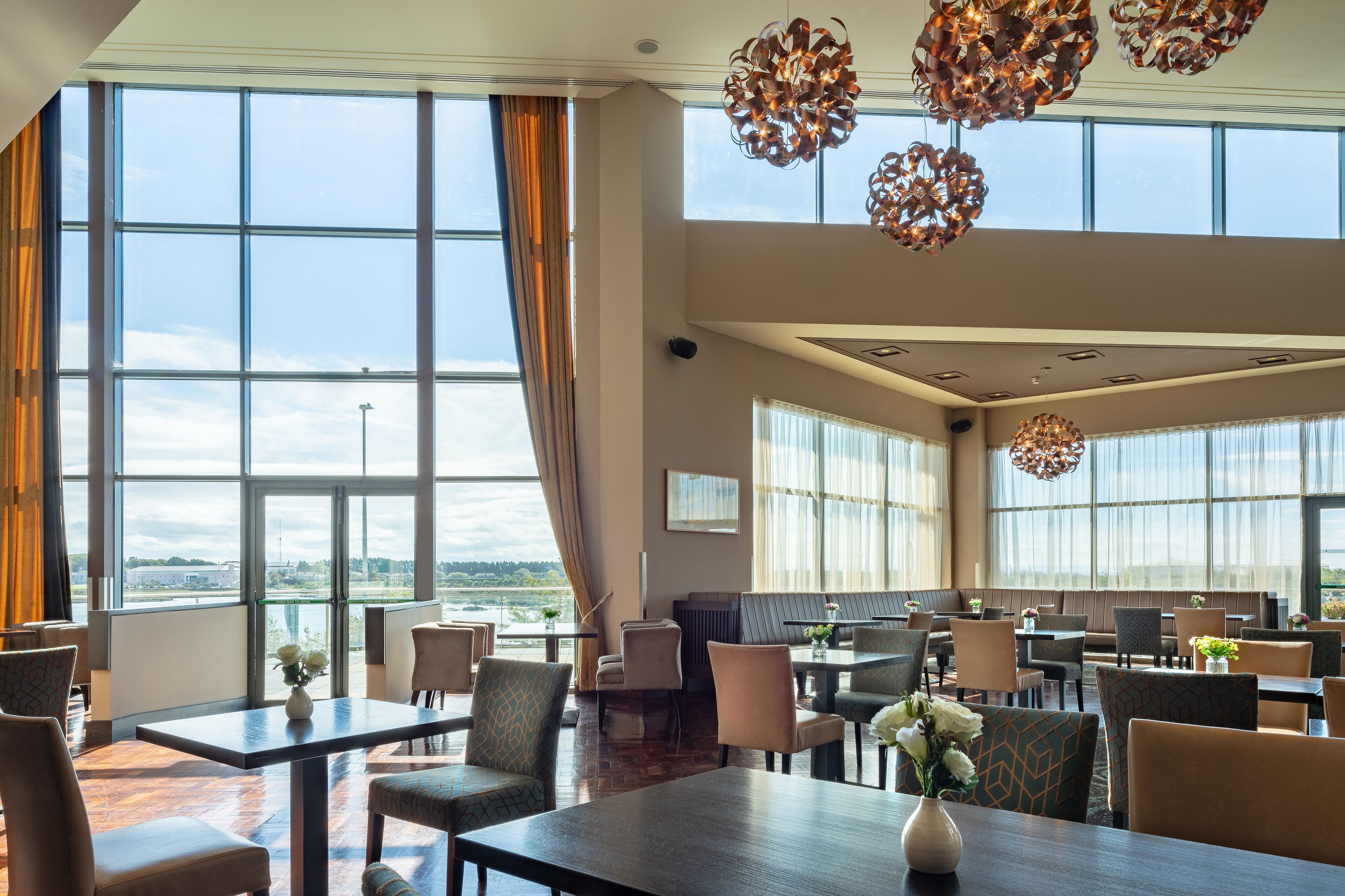 En rummelig hotelrestaurant med store vinduer, moderne lysekroner og behagelige siddepladser.