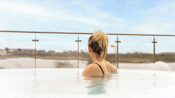 A person in a hot tub with a view of a body of water and distant buildings.