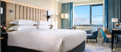 A hotel room with a large bed, a desk, a chair, and a view of the outdoors.