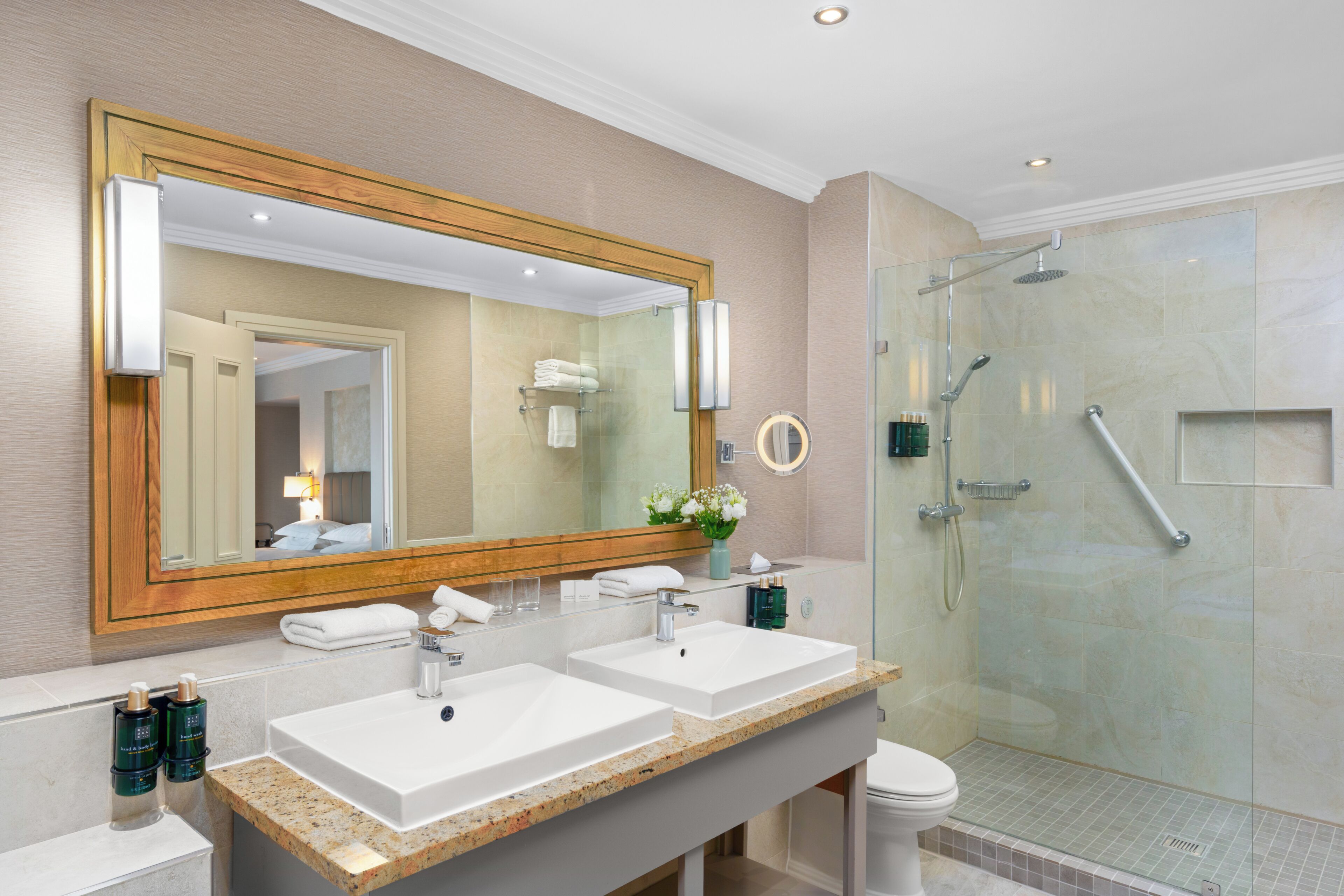 A modern bathroom with two sinks, a large mirror, and a glass-enclosed shower.