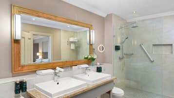 A modern bathroom with two sinks, a large mirror, and a glass-enclosed shower.