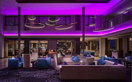 A modern lobby with a bar area, seating arrangements, and a view of the cityscape.