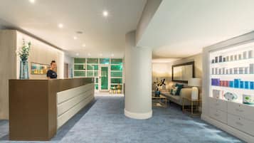 A reception area with a reception desk, a large pillar, a seating area with a sofa and a lamp, and a display of products on shelves.