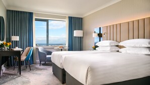 A hotel room with a large bed, a desk with a chair, a window with curtains, and a view of the sea. - The Galmont (Galway)
