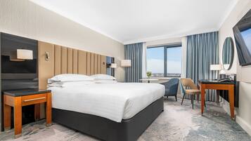 A hotel room with a large bed, a desk, a chair, a small table, and a window with curtains.