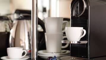 A coffee machine with a cup of coffee on the counter, a stack of white cups, and a blue napkin.