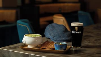 A tray with a bowl of soup, a slice of bread, a small bowl of butter, and a glass of Guinness beer on a table.