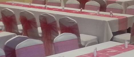 A banquet hall with rows of tables covered in white tablecloths and pink sashes, equipped with white chairs and name placards.