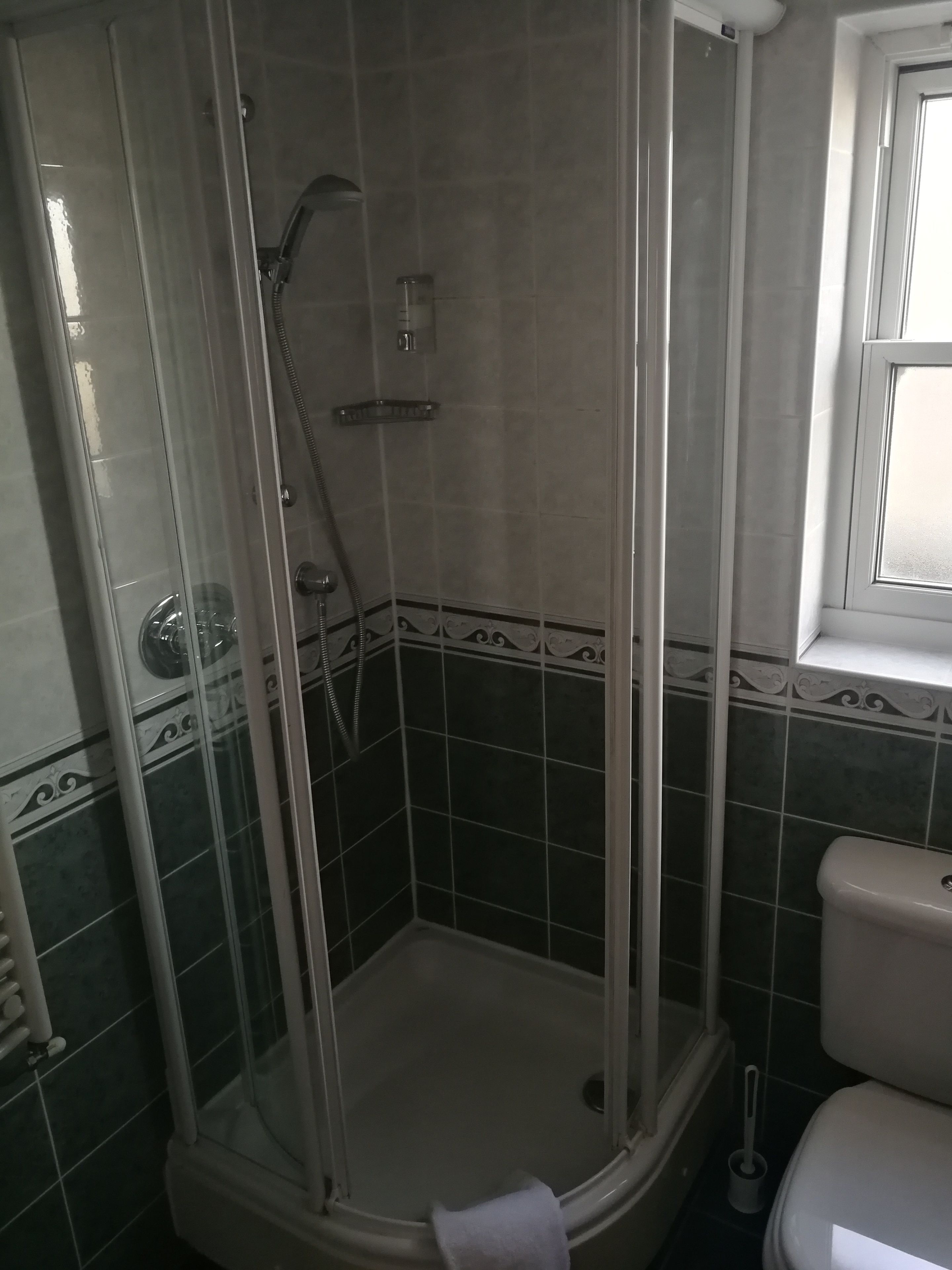 Un baño con ducha separada por mampara de vidrio, inodoro y ventana.