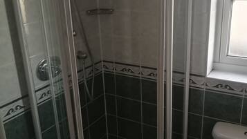 Un baño con ducha separada por mampara de vidrio, inodoro y ventana.