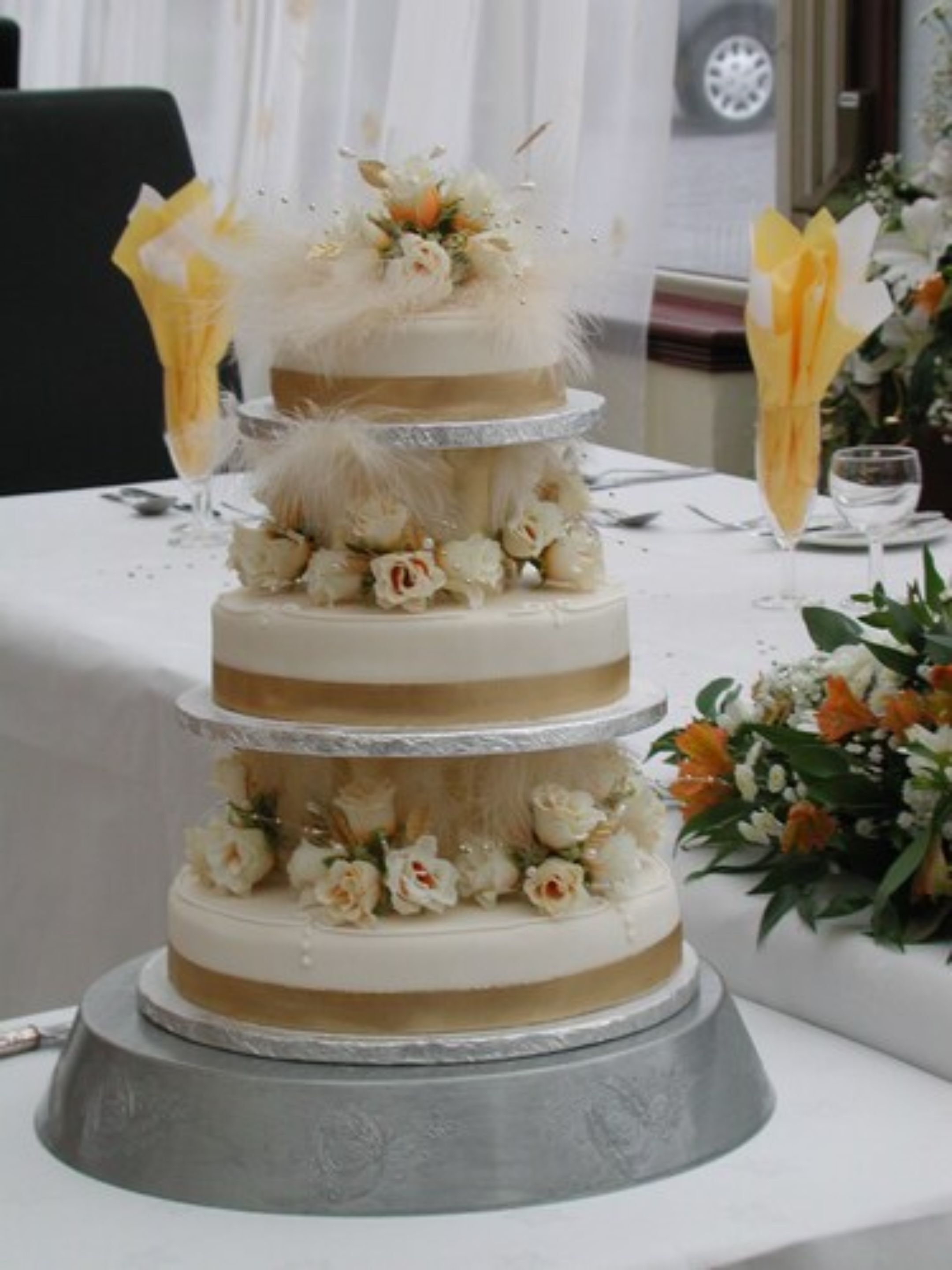 A multi-tiered wedding cake with floral decorations, placed on a table with a white tablecloth.