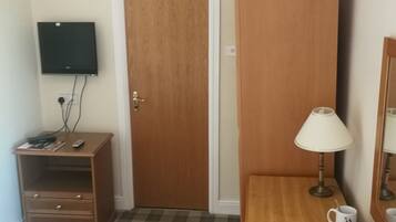 Habitación de hotel con un armario de madera, un escritorio pequeño con lámpara, un televisor montado en la pared y suelo a cuadros.