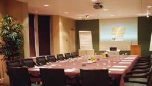 Un salón de conferencias con una larga mesa, sillas, una pantalla de proyector y una pizarra para presentaciones.