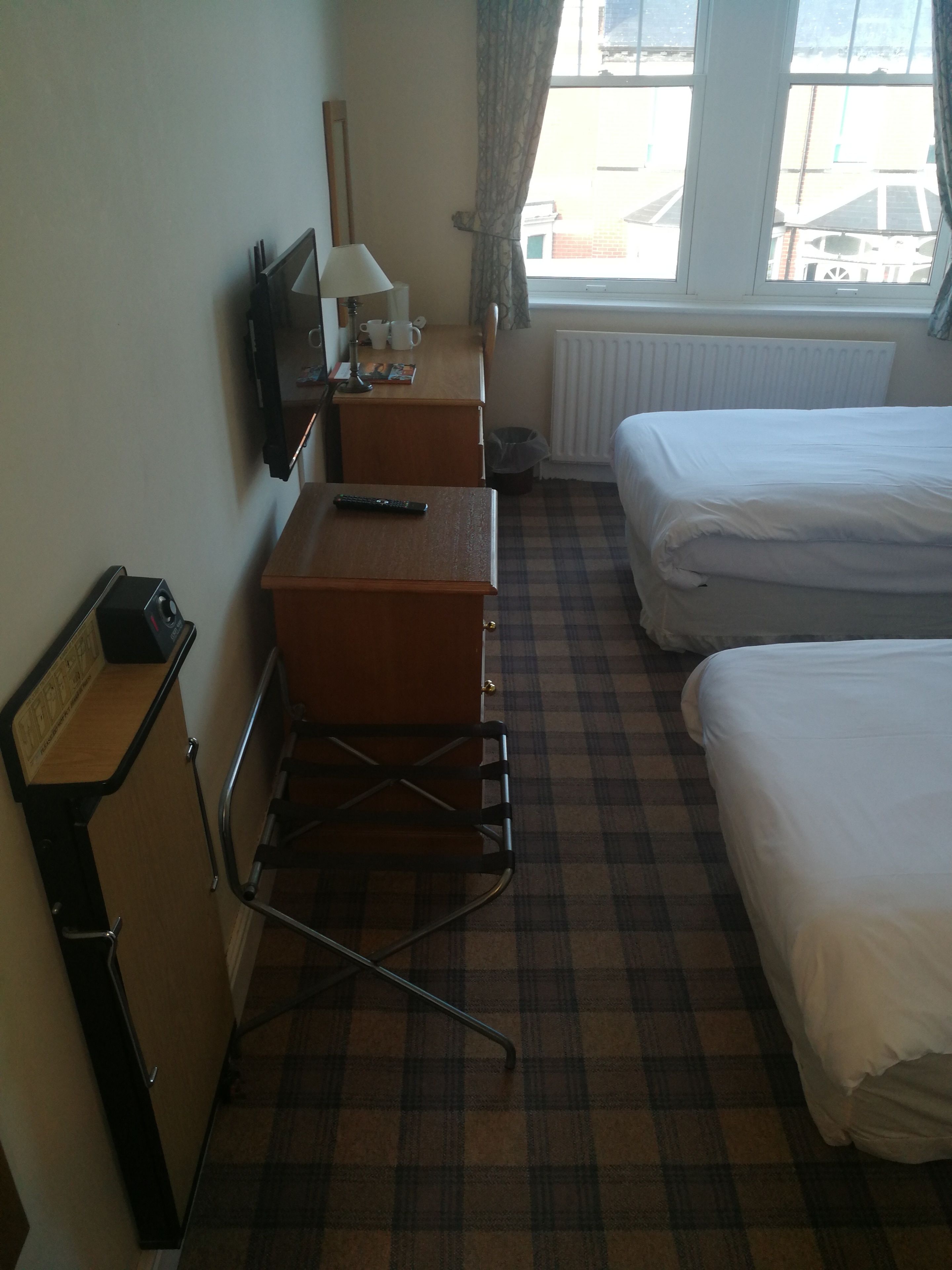 A hotel room with a bed, a desk, a chair, a radiator, and a window with a view of buildings.