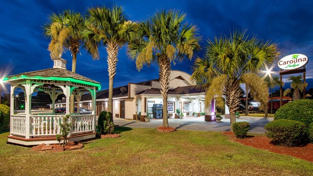 A gazebo with a white railing and a palm tree in front of a building with a sign that reads "Carolina Inn." - Carolina Lodge (Barnwell)