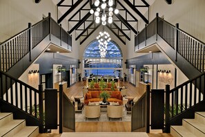 A spacious lobby with a central seating area, a staircase, and a large arched window offering a view. - Courtyard Hotel Gqeberha (Gqeberha (Port Elizabeth))