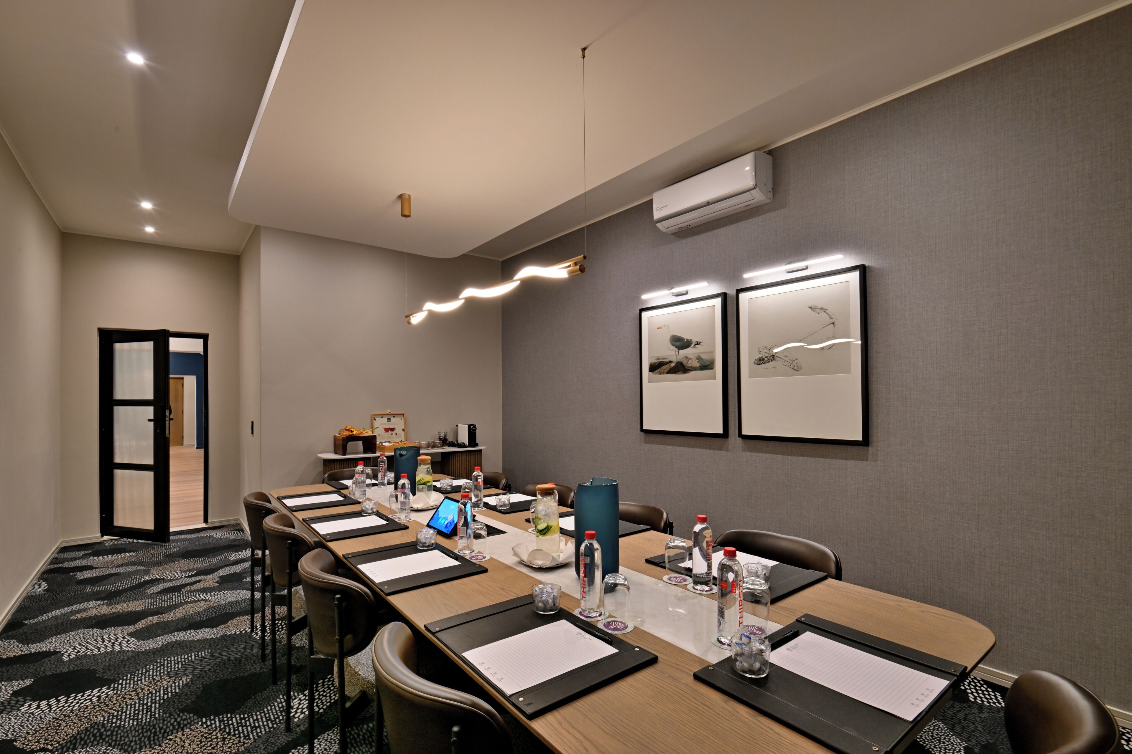 A conference room with a long table, chairs, water bottles, a laptop, and framed pictures on the wall.