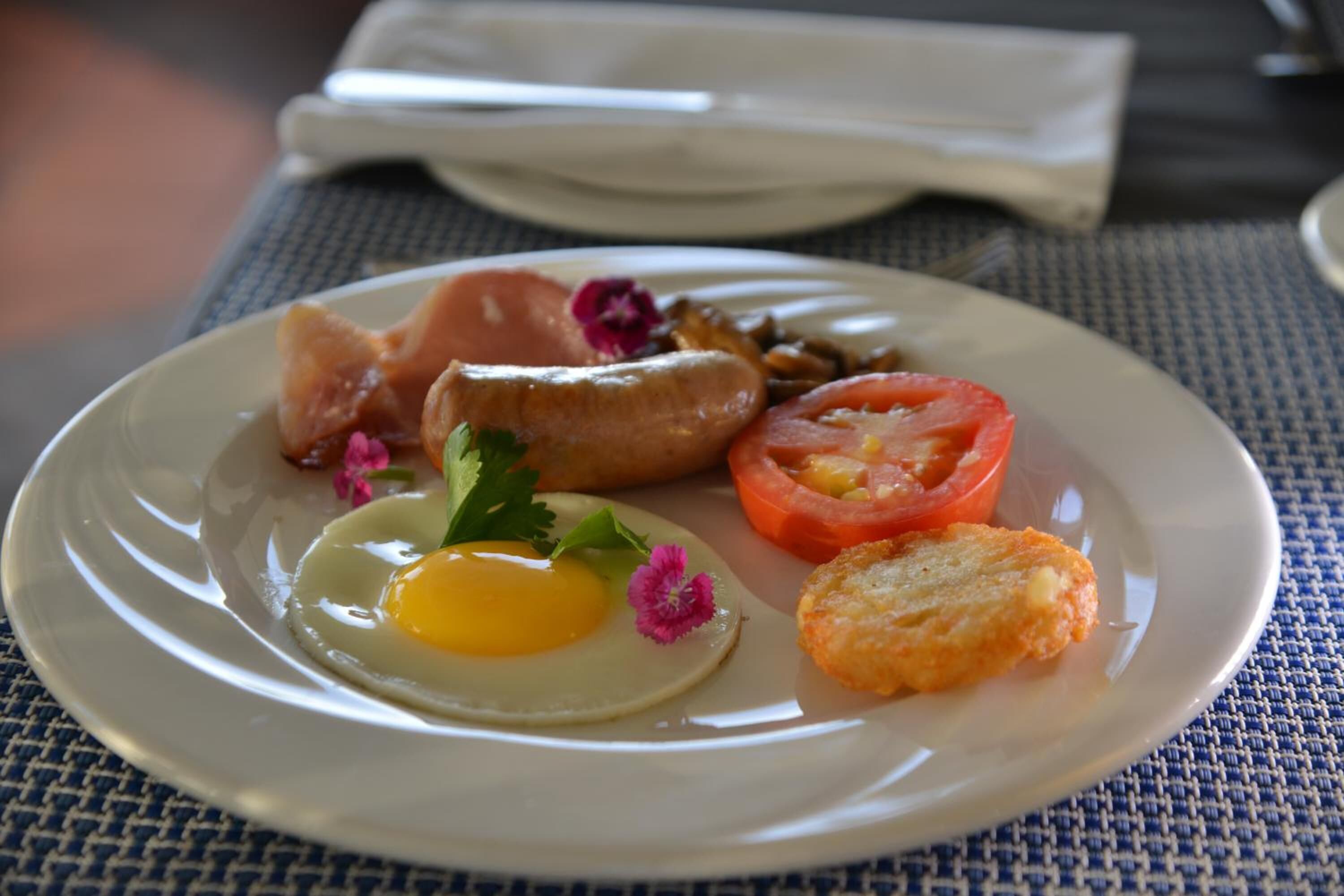 Un plato de comida para el desayuno que incluye un huevo, salchicha, tomate y patatas ralladas.