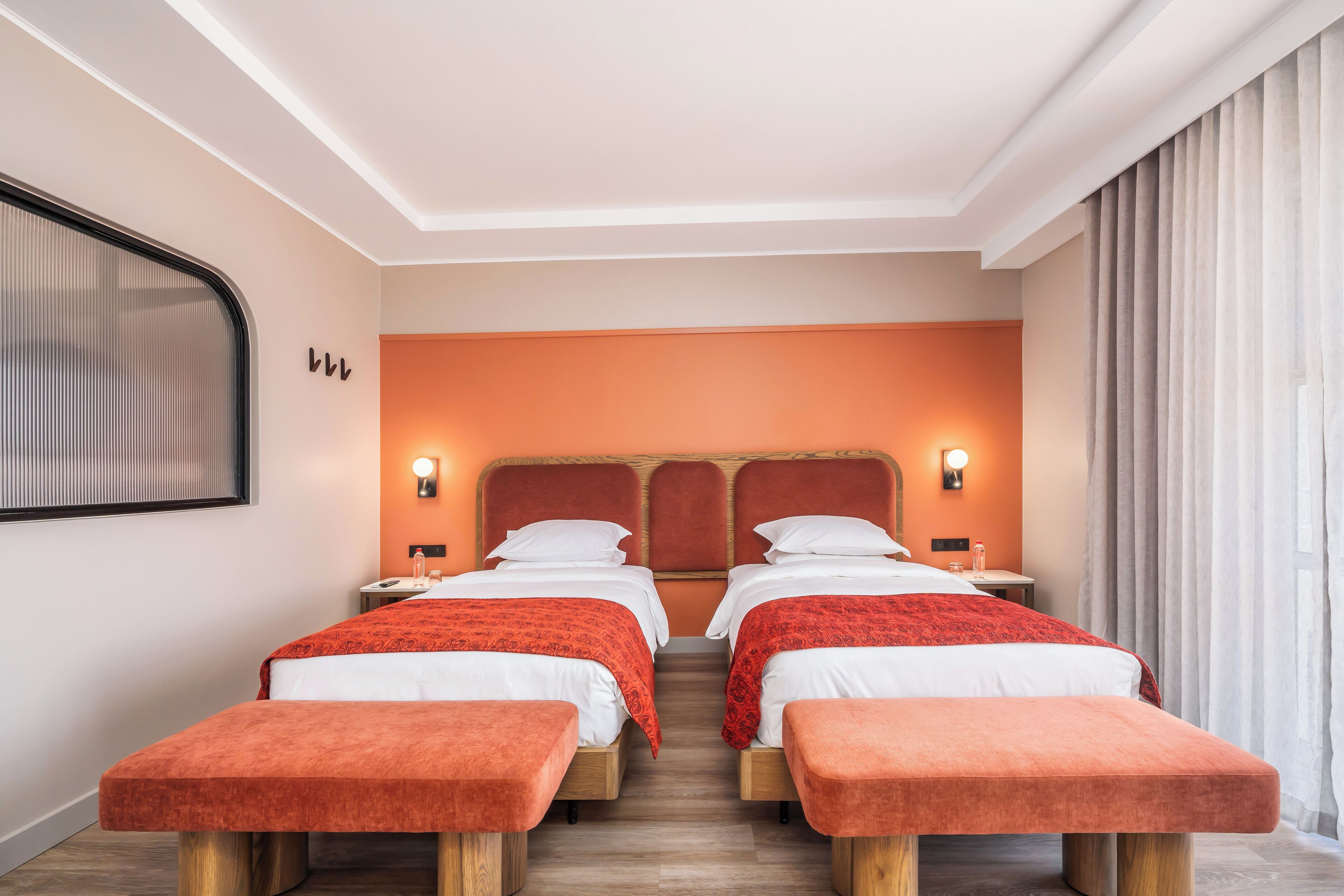 A hotel room with two beds, each with a red bedspread, wooden headboards, and bedside tables with lamps.