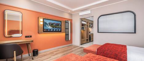 Une chambre d’hôtel moderne avec un bureau en bois, un grand miroir, un téléviseur à écran plat et deux lits avec une literie à motifs rouges.