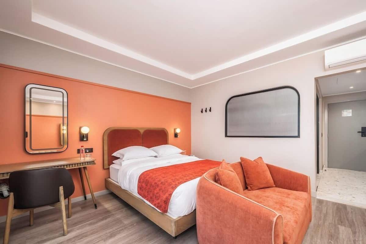 Una habitación de hotel con cama, escritorio, silla, sofá y un espejo grande.
