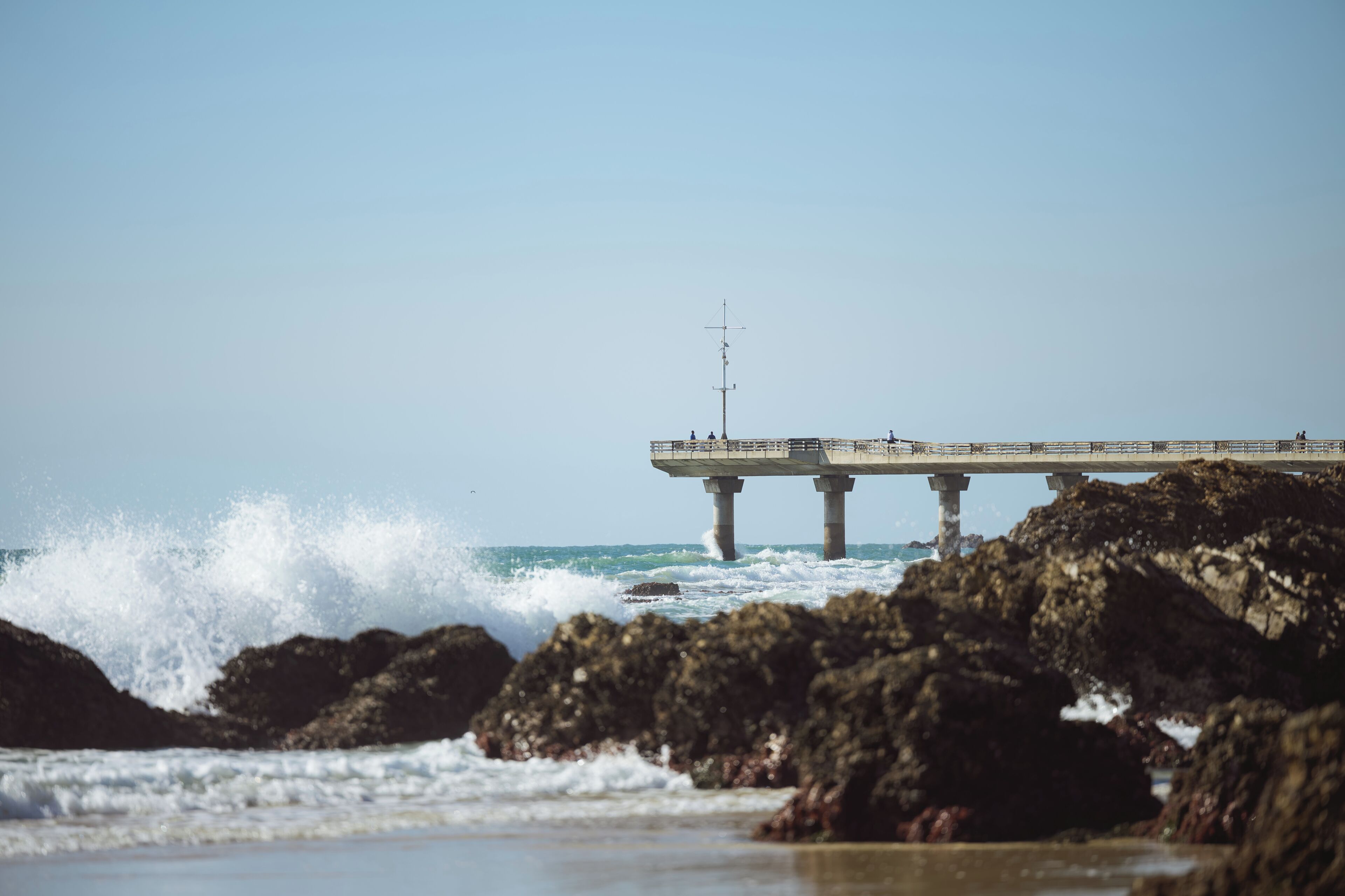 A pier extending into the sea with waves crashing against rocks.