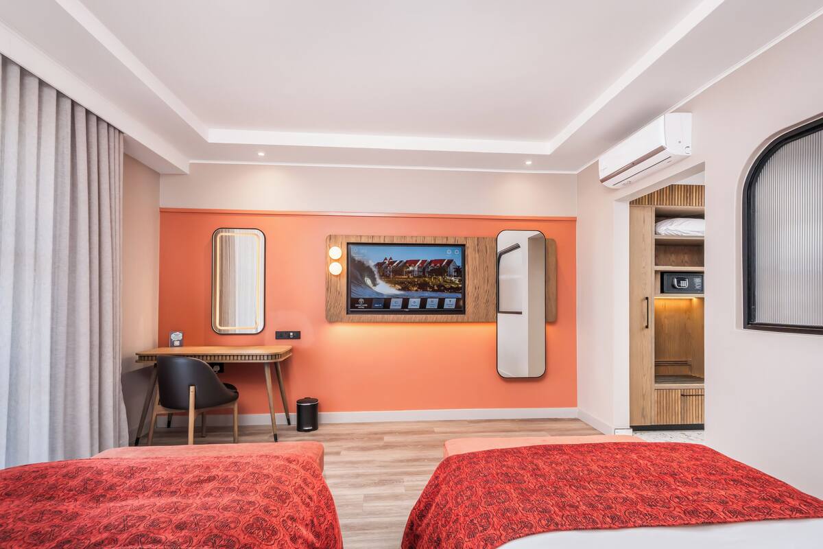 Habitación de hotel con dos camas, un escritorio, una silla, un televisor y un armario.