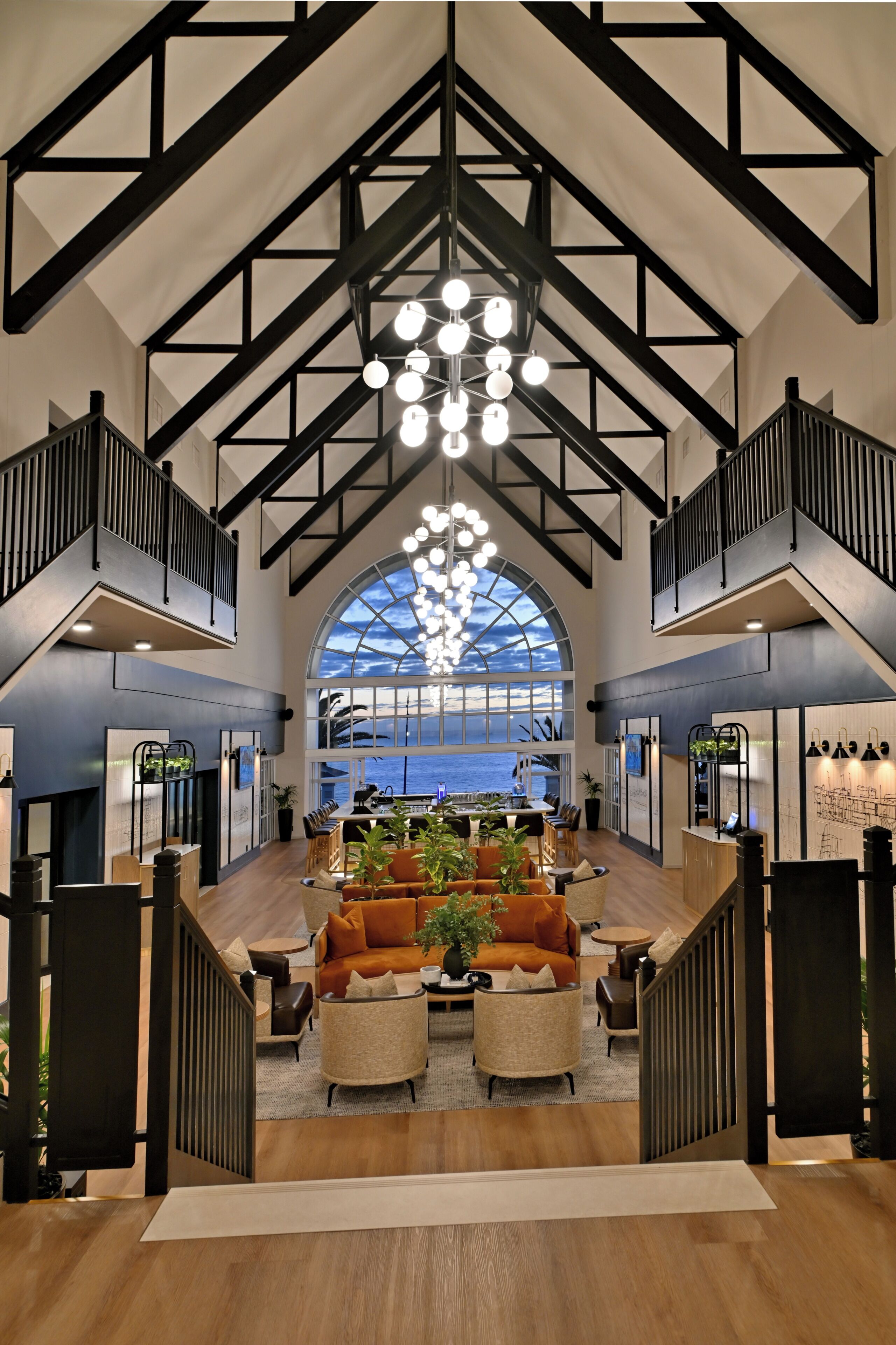 Een ruime lobby met een hoge plafond, een trap en een groot rondboogvenster met uitzicht op zee.