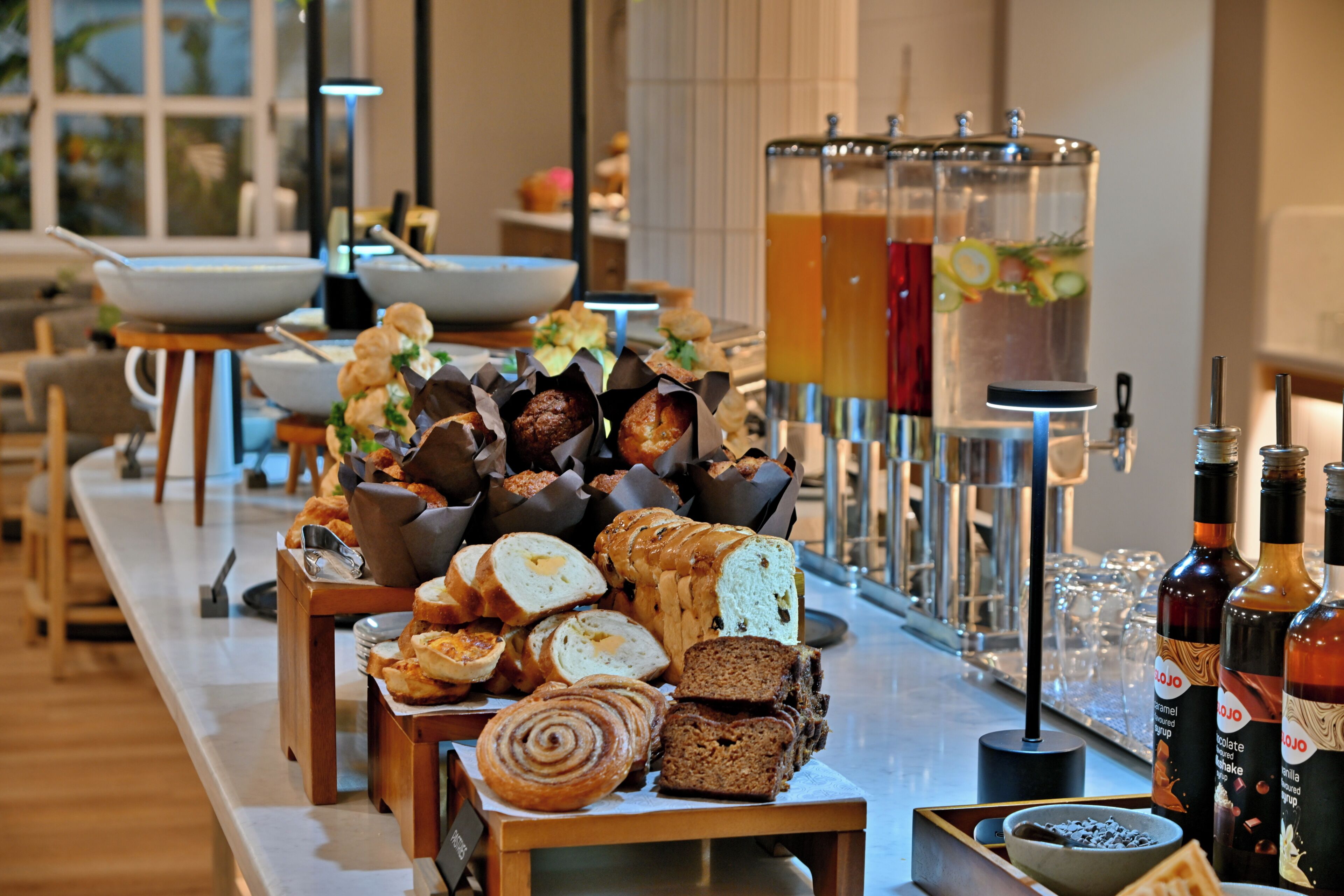 A buffet with various breads and pastries, a beverage station, and a view of the room.