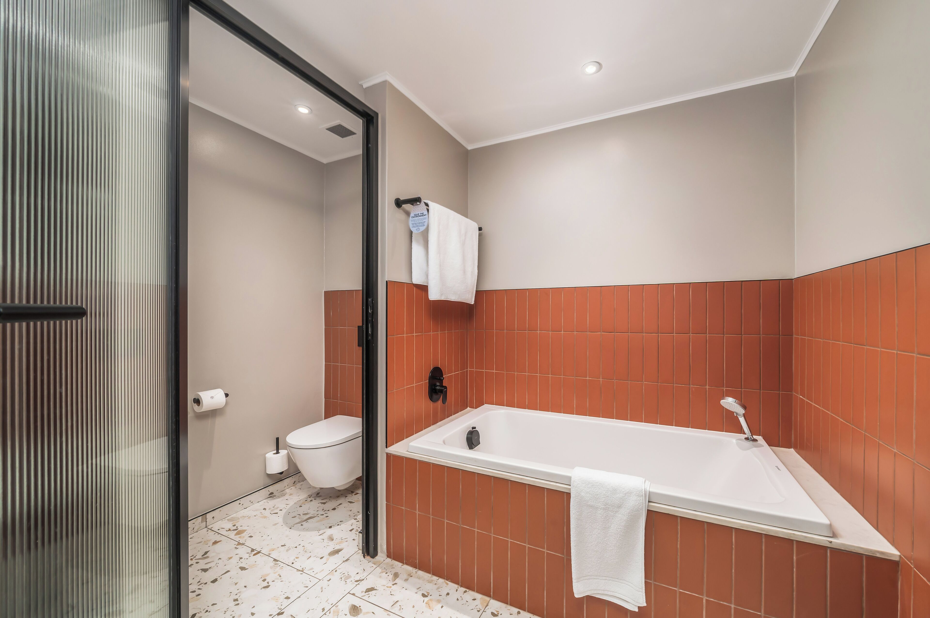 A modern bathroom with a bathtub, toilet, and glass shower enclosure.