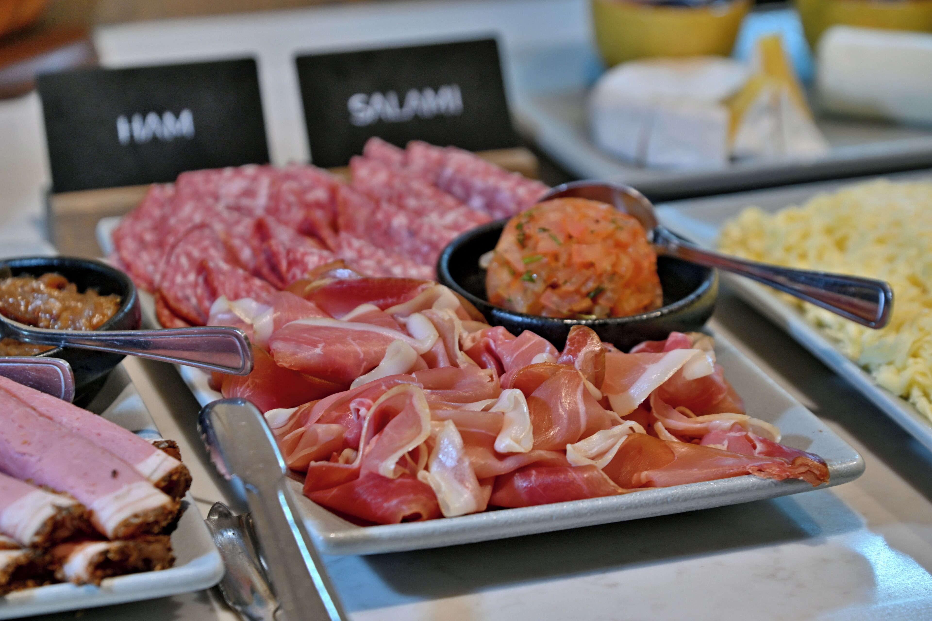 A variety of meats including ham and salami on a buffet table.