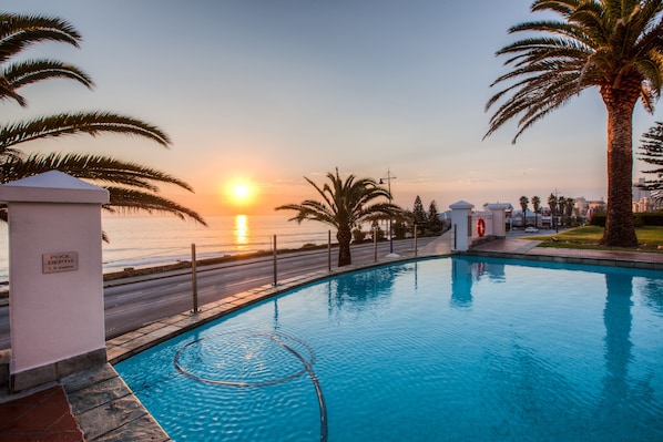 Una piscina con vista al atardecer, palmeras y un cartel que indica una profundidad de 1,5 metros.