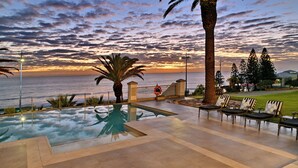 A pool area with a view of the ocean at sunset, palm trees, and outdoor seating. - Courtyard Hotel Gqeberha (Gqeberha (Port Elizabeth))