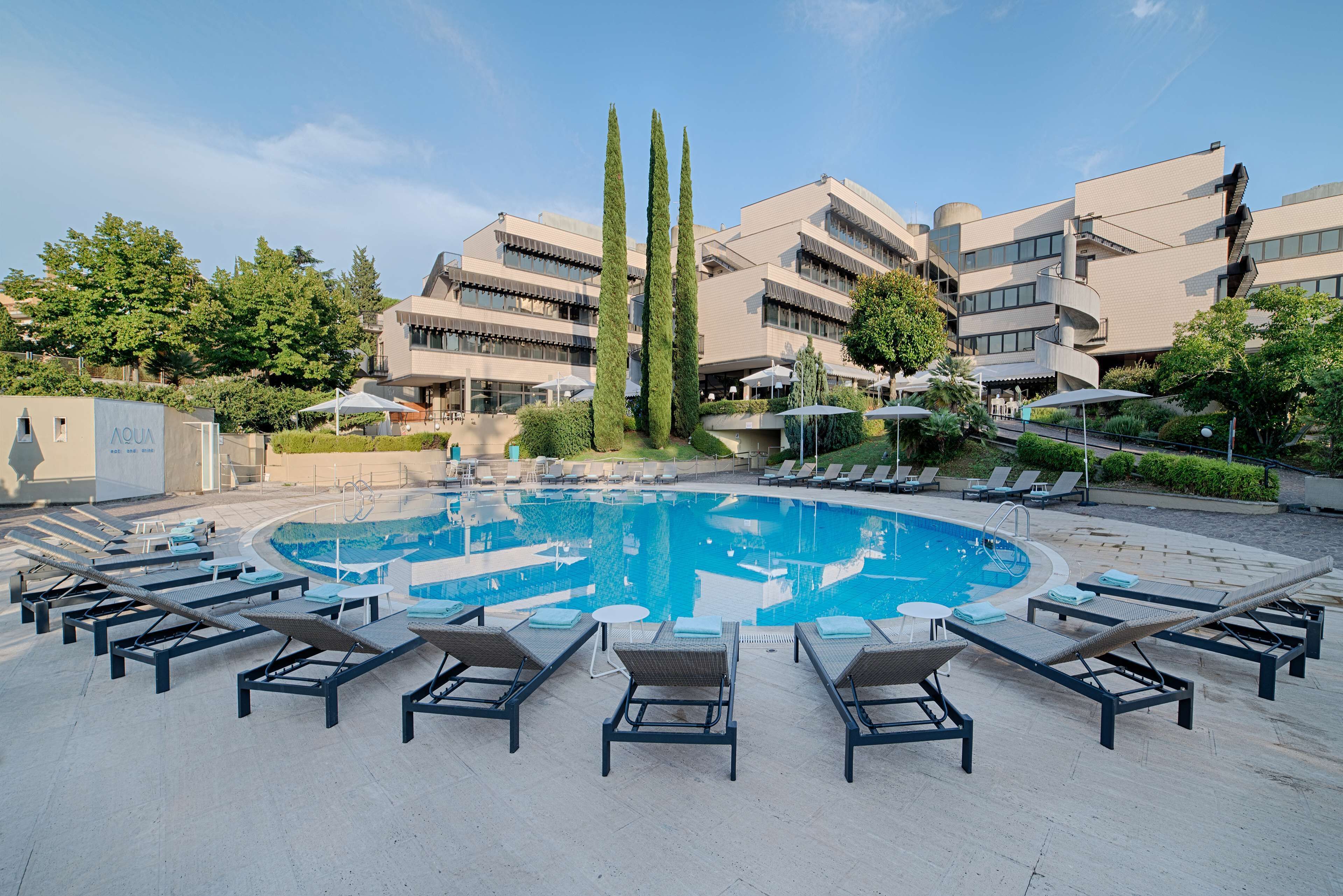 A swimming pool with sun loungers and a modern building in the background.