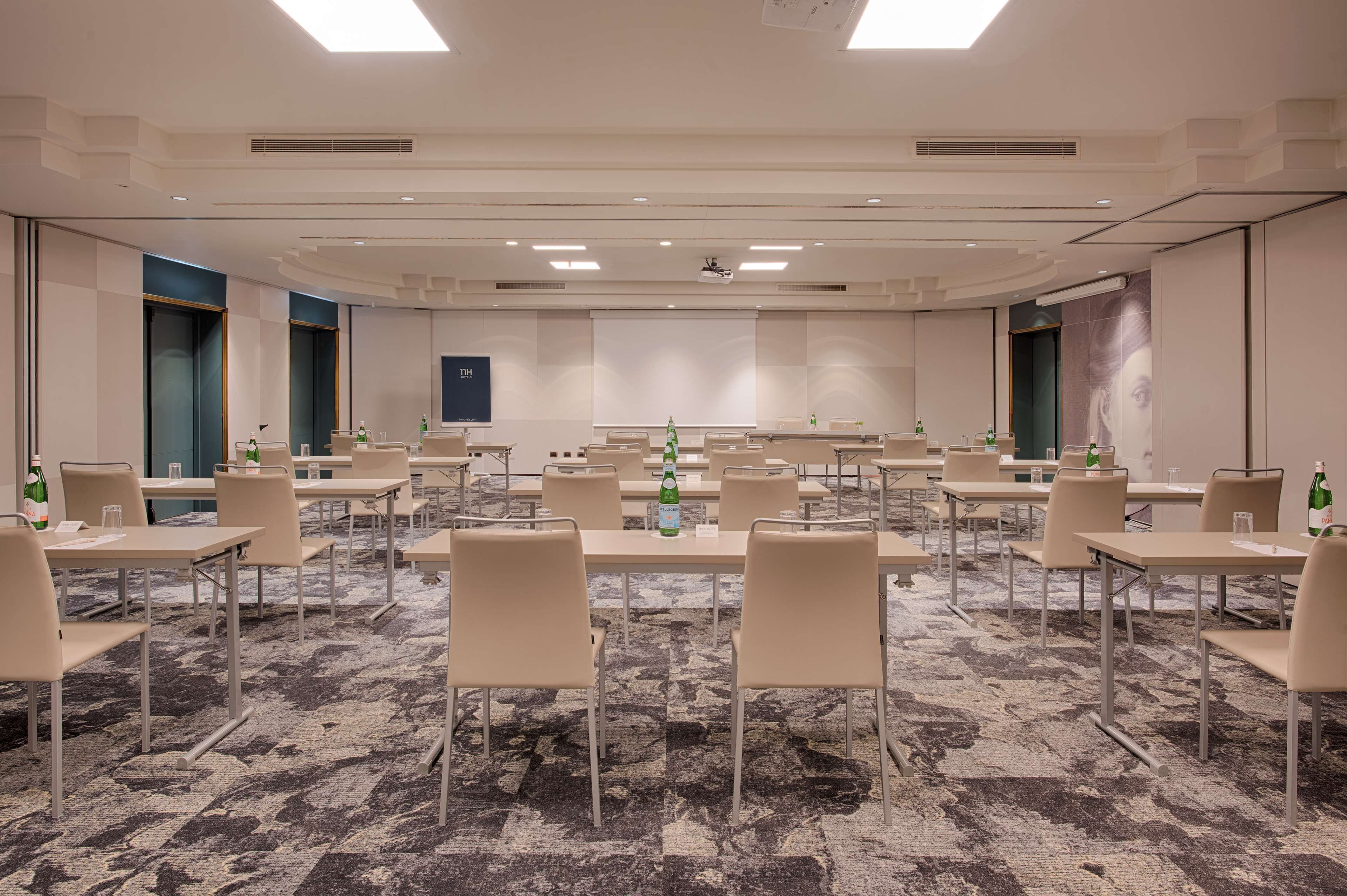 A conference room with a carpeted floor, multiple tables, and chairs, equipped with water bottles and glasses.