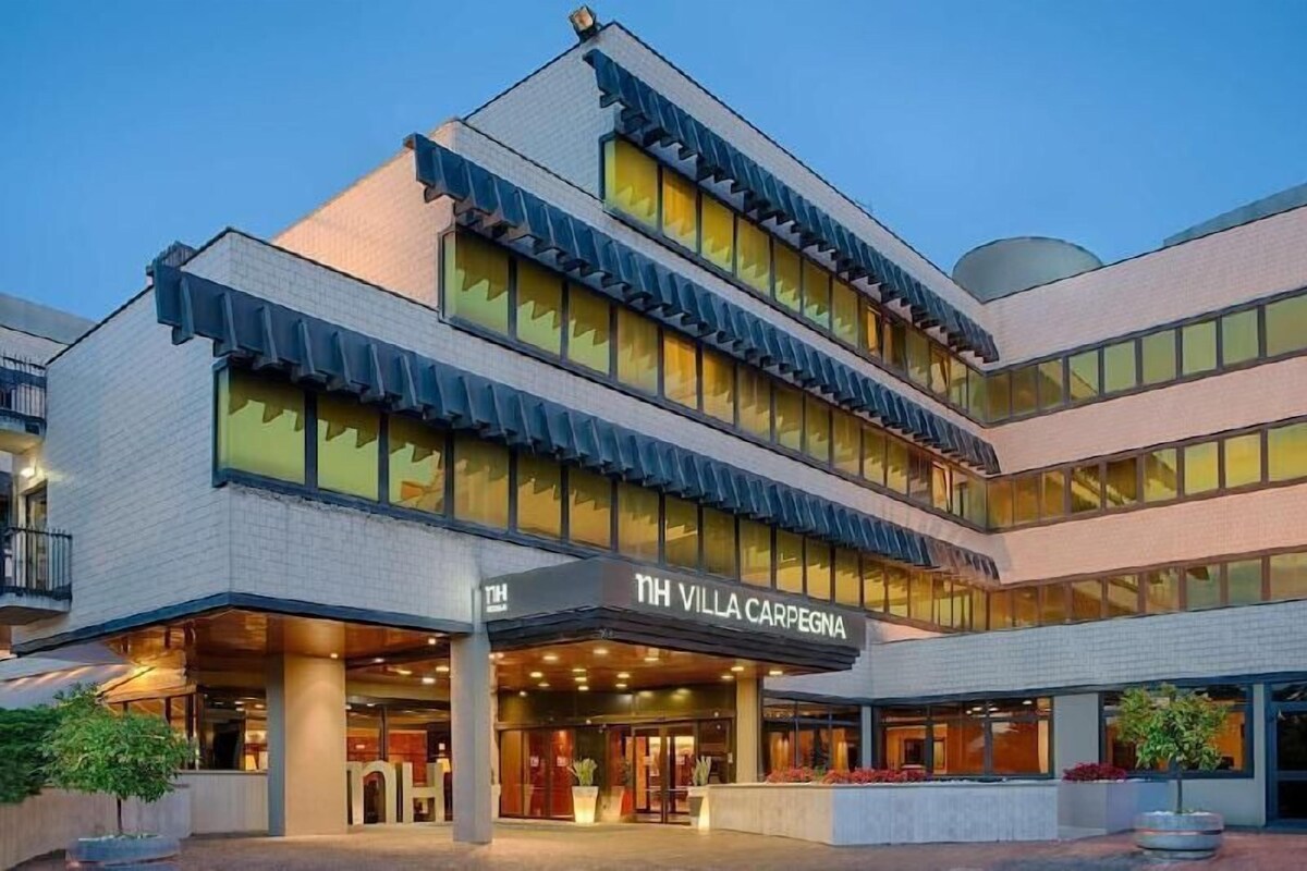 Un hotel de varios pisos con diseño moderno, que destaca por su entrada principal y una amplia zona exterior con mesas y sillas.