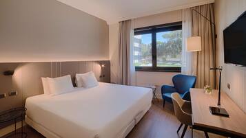 A hotel room with a large bed, a desk with a chair, a TV, and a window with curtains.