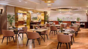 A spacious restaurant with multiple dining tables and chairs, a bar area, and potted plants.