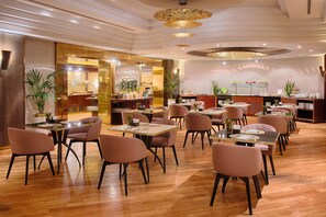 A spacious restaurant with multiple dining tables and chairs, a bar area, and potted plants.