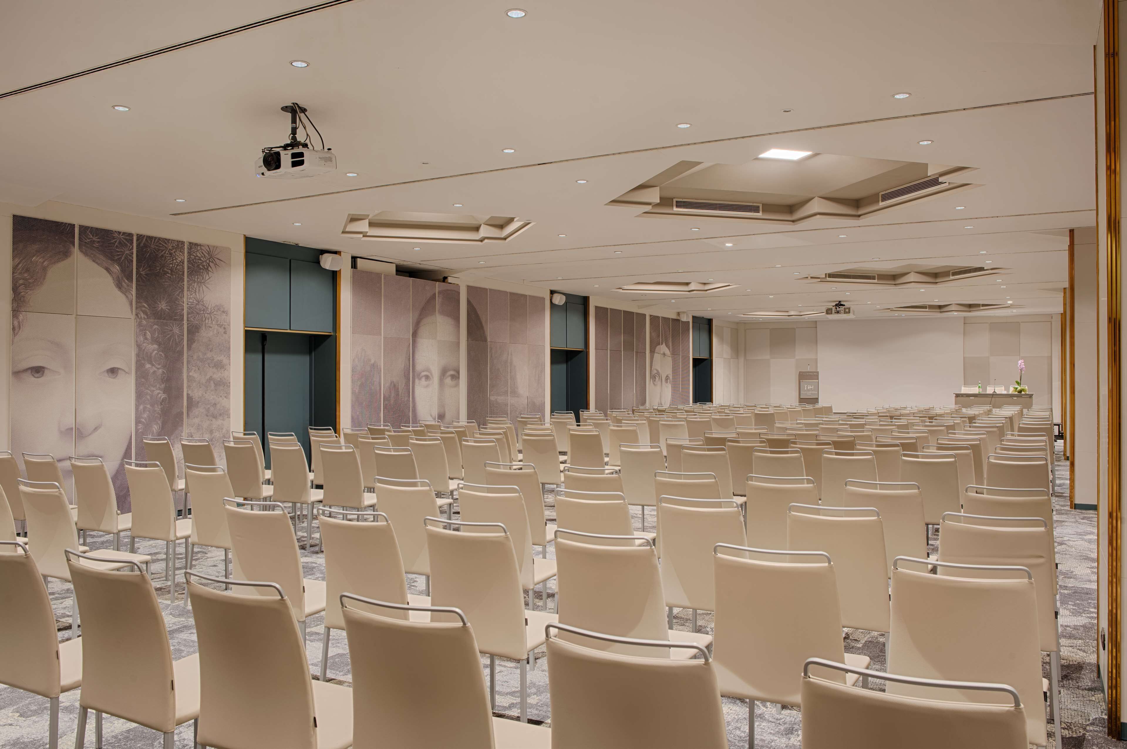 Un salón de conferencias con filas de sillas, un proyector y una pantalla grande.