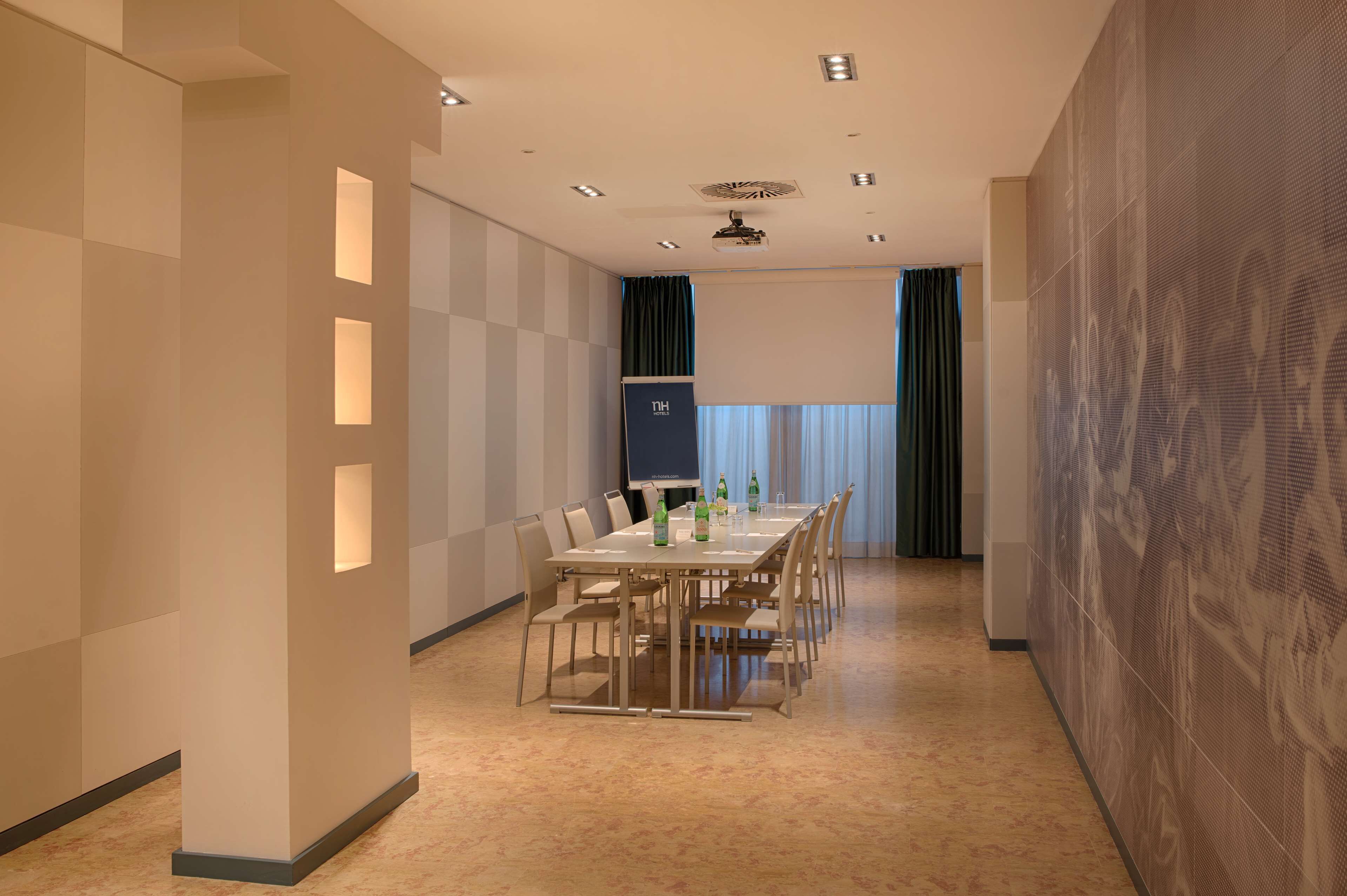 A conference room with a long table, chairs, a projector screen, and a large patterned wall.