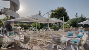 Une terrasse extérieure avec des meubles en osier blanc, des parasols et un escalier en colimaçon.