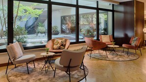 Un intérieur moderne avec de grandes fenêtres, un sol en pierre et plusieurs coins salon dotés de tables rondes.